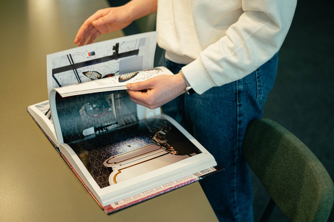 An adult man flipping through a design magazine indoors, showcasing creative and modern interior elements.
